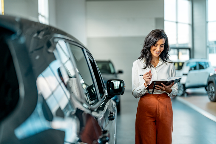 Person reviewing paperwork beside a new car, representing car purchase tax deductions, business vehicle expenses and ATO rules for claiming work-related car expenses in Australia.